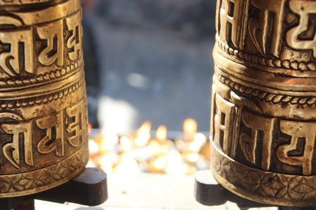 Gouden gebedsmolens met Indic script, op een achtergrond van vlammen en religieuze sfeer.
