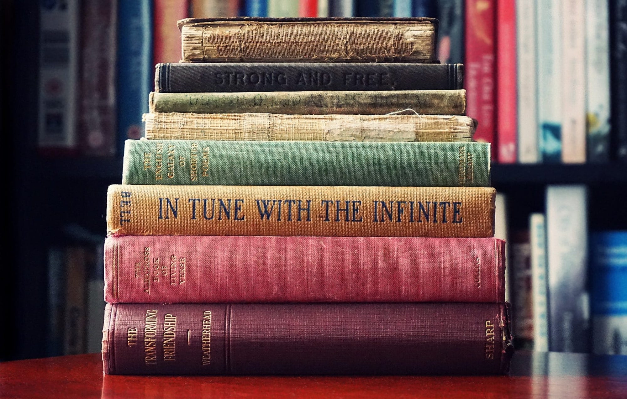 Stack of vintage books titled 'In Tune with the Infinite' and 'Strong and Free' on a wooden table.