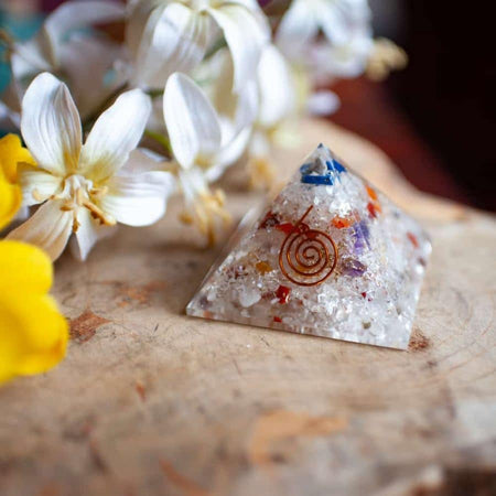 Orgonite pyramid with colorful crystals and flowers on a wooden surface, symbolizing spiritual energy.